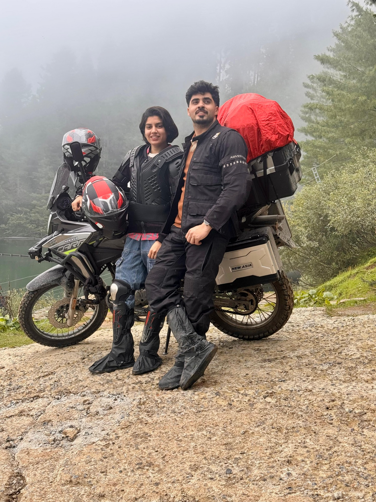 Two riders with their helmets and motorcycle beside a misty forest