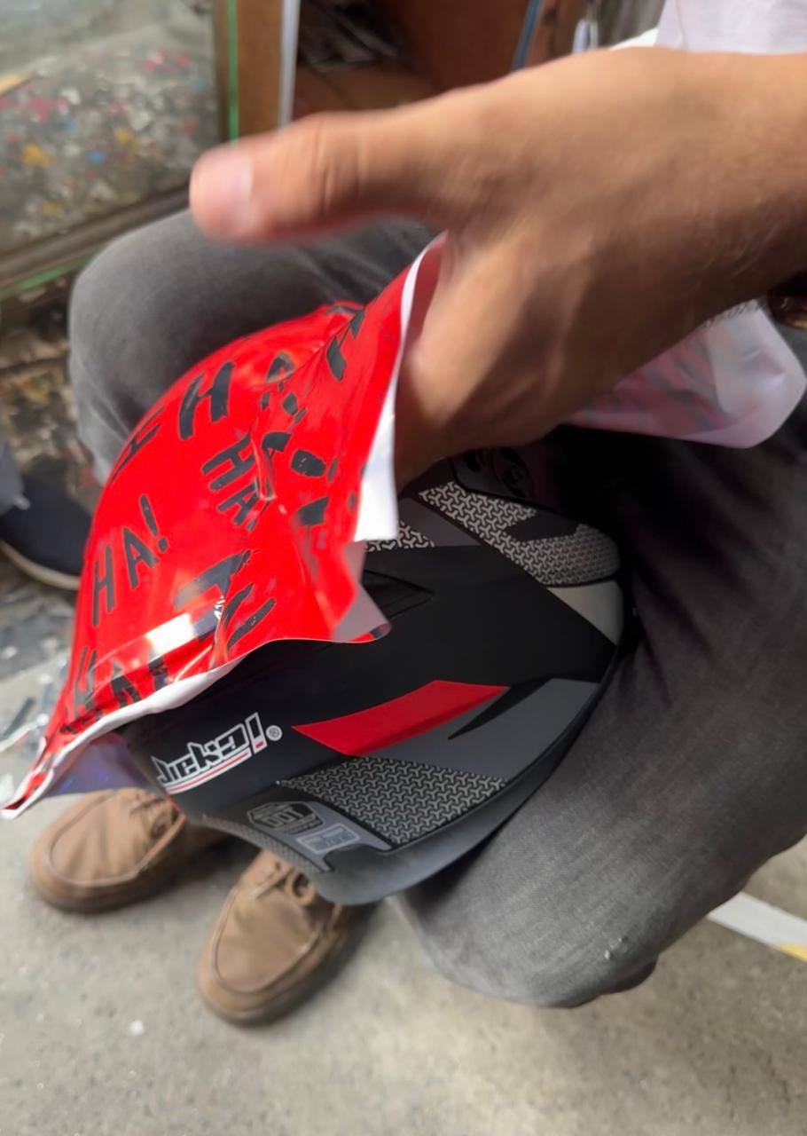 Unlaminated red printed vinyl being handled around a helmet during fitting or removal